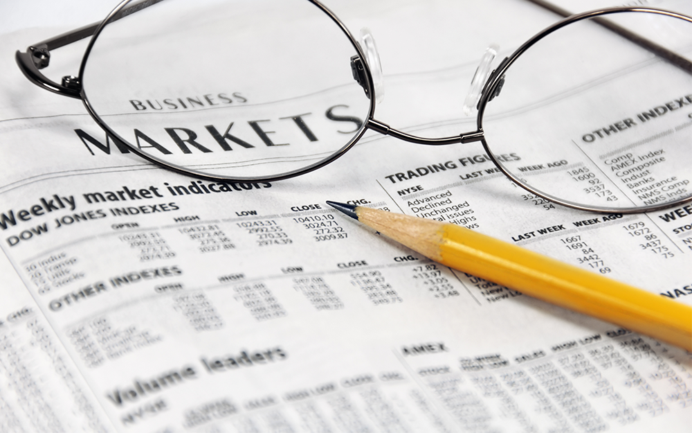 An eyeglasses and yellow pencil place on a newspaper in a business/markets section.